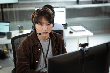 Focused customer support representative wearing headset works attentively at computer in modern...