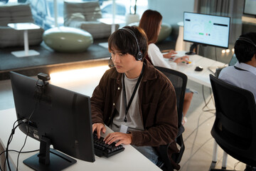 Focused tech support professional wearing headset works at computer in modern office environment, assisting customers with their inquiries. workspace is equipped with monitors and ergonomic chairs