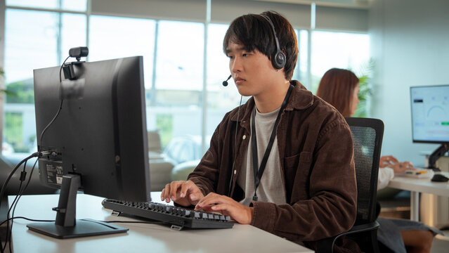 Focused tech support professional working at desk, wearing headset, typing on keyboard, and assisting customers in modern office environment