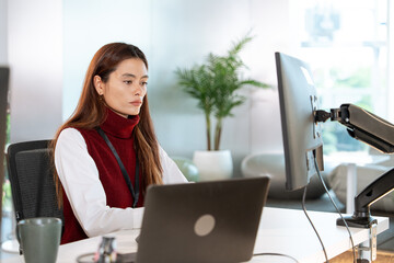 Focused woman working at desk with laptop and monitor in modern office environment, showcasing professional and tech driven atmosphere for customer support tasks