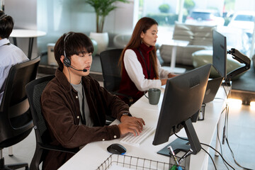 Focused customer support team working in modern tech office, with man wearing headset typing on keyboard and woman in background assisting customers