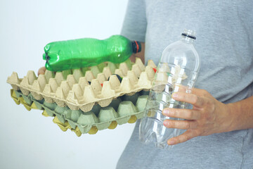 Person sorting recyclable materials: empty plastic bottles and used paper egg trays. Waste separation and eco-friendly lifestyle. Close-up view of hands managing household waste in responsible way.