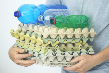 Waste sorting: person holding stack of egg trays and plastic bottles for recycling. Caring for the environment in daily actions: collection of paper and plastic for reuse. Eco-friendly lifestyle