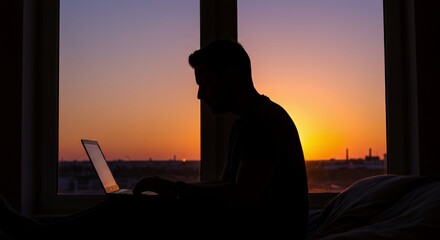 Silhouette of a person working on a laptop at sunset, enjoying the view from a window.
