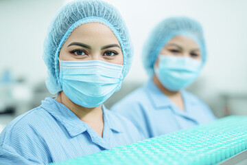 Two healthcare workers in protective masks and hair nets during a medical or laboratory procedure, focusing on safety and hygiene.