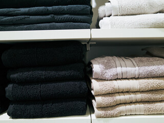 Stack of black and white towels is on a shelf next to a stack of white towels