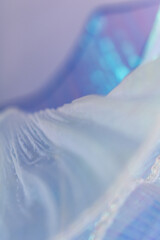 Textured close-up of airy, iridescent mesh in pastel blue tones with translucent folds and layered...