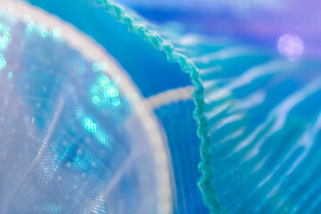 Close-up of shimmering light blue mesh fabric with delicate folds and semi-transparent texture,...