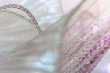 Close-up of translucent iridescent fabric with glittering edges in pastel pink and blue, flowing...