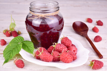 Jar of raspberry jam on white wooden background.
