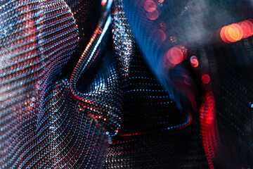 Close-up of shimmering metallic textile with red and blue reflections, abstract folds, and dotted...