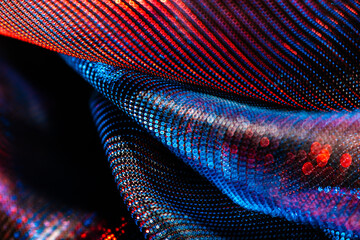 Close-up of shimmering, metallic fabric with red and blue reflections, abstract folds, and dotted...