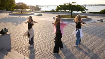 Four women energetically practice street dance on a sunny riverside promenade. Concept of urban...