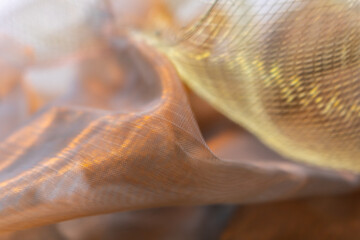 Abstract close-up of translucent flowing fabric with warm golden light reflections and soft mesh...