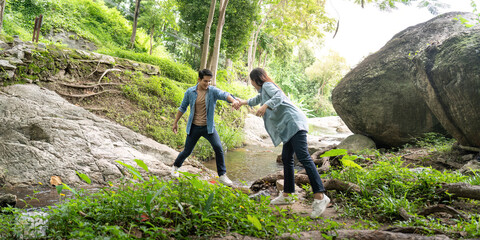 Couple navigating rocky terrain. Young man and woman helping each other across a stream in a forest.