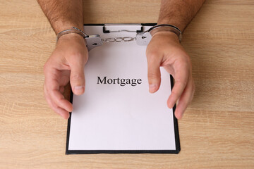 A man in handcuffs holds a document with the inscription 