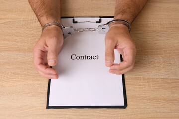 A man in handcuffs holds a document with the inscription 