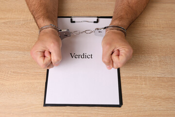 A man in handcuffs holds a document with the inscription 