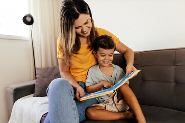 Smiling mother and son enjoy reading a book together on the couch