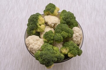 Fresh broccoli and cauliflower in bowl on fabric surface