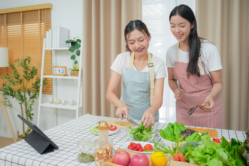 Asian young two women cooking salad in kitchen. Active beautiful girl feel happy and enjoy eating vegetables healthy foods to diet and lose weight for health care in house	