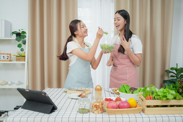 Asian young two women cooking salad in kitchen. Active beautiful girl feel happy and enjoy eating vegetables healthy foods to diet and lose weight for health care in house	