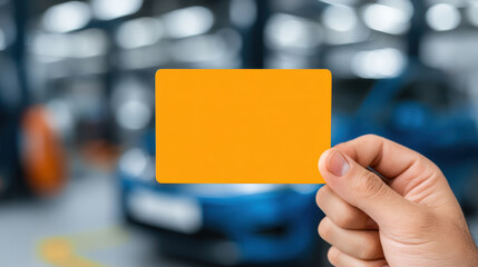 Orange card held by hand with blurred car background in garage or workshop