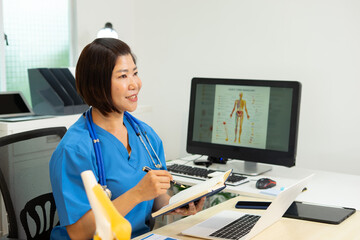 Medical professional writing notes with stethoscope and anatomy chart on computer