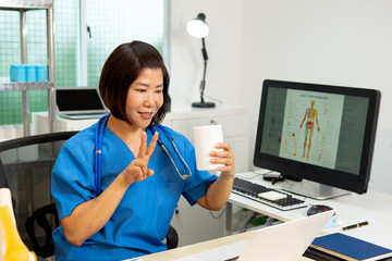 Female doctor video call with medicine cup, smiling nurse in blue scrubs showing peace sign