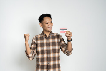 A cheerful man in casual attire smiles and raises his fist in excitement while holding a payment card, symbolizing financial success, achievement, or purchasing power.