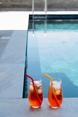 Minimalistic photo of two homemade Aperol spritz cocktails with ice and colorful silicone straws...