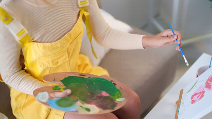 Young Asian woman painting art with brush holding palette with various color for creative ideas concept and painting hobby on canvas