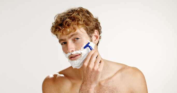 Portrait, shaving cream and man with razor, beauty and grooming on white studio background. Face, person and model with beard care, facial product and wellness with hair removal, foam and epilation