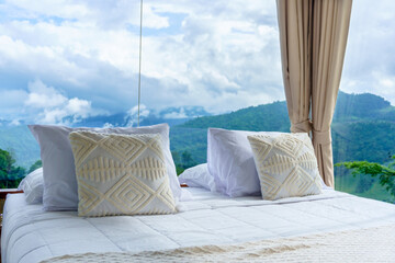 Comfortable bed with white pillows and decorative cushions facing a panoramic mountain view through floor-to-ceiling windows. A perfect escape into nature and tranquility.