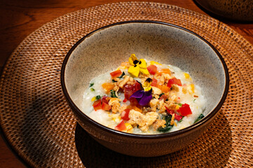 A close-up of a bowl of gourmet porridge, garnished with colorful vegetables and edible flowers.