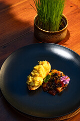 Gourmet breakfast: scrambled eggs and vegetable medley served on a dark plate.