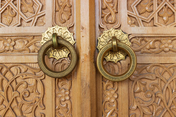 Close-up of pair of symmetry old brass hanging ring door knobs covered with floral ornament on carved wooden gate