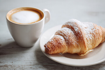 Cornetto pastry rests beside a creamy cappuccino in a white ceramic cup