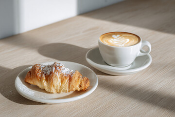 Cornetto pastry rests beside a creamy cappuccino in a white ceramic cup
