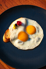 Three fried eggs on a dark plate, garnished with flowers and served with toasted bread.