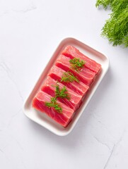 Freshly cut tuna steaks garnished with herbs on a white plate, set against a light background