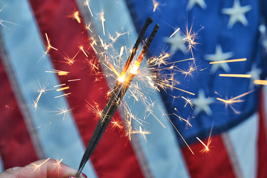 Holding a sparkler in front of an American Flag to celebrate the 4th of July Independence Day - Powered by Adobe