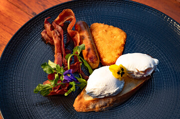 A gourmet breakfast platter featuring bacon, sausage, hash browns, and poached eggs on toasted...