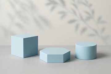 Blue cube, hexagon, and cylinder create an elegant product display set against a wall with leaf shadows