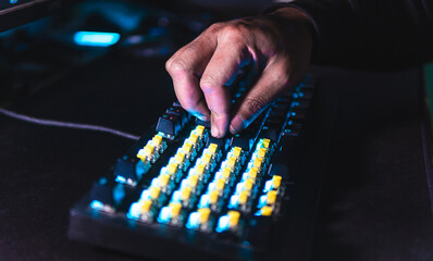 Close-up of hands installing keycaps on an RGB mechanical keyboard. Yellow switches and blue...