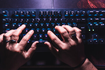Top-down view of hands typing on a mechanical keyboard with glowing keys. Suitable for tech,...