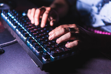 Close-up hands typing on a mechanical keyboard with LED backlight in a dark room. Shallow depth of...