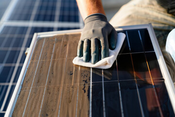 Cleaning a dirty solar panel. A gloved hand uses a cloth to clean a dusty photovoltaic panel, improving its efficiency. Concept of maintenance for renewable energy.