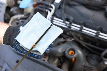 Worker checking motor oil level in car with dipstick, closeup