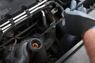 Fototapeta premium Worker checking motor oil level in car with dipstick, closeup